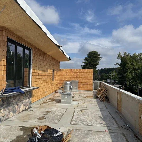 Rooftop patio with stone and wooden exterior walls under clear blue sky during construction.
