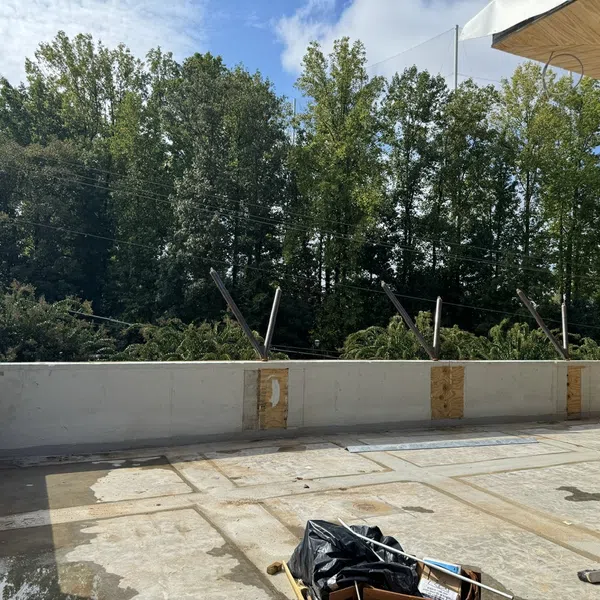 Empty rooftop terrace under construction with safety railings and trees in the background on a sunny day