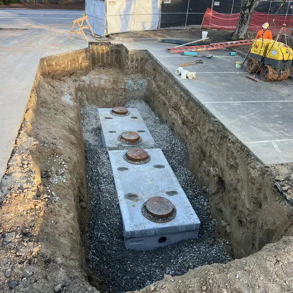 Large rectangular concrete septic tanks installed in a deep excavation at a construction site with surrounding equipment.