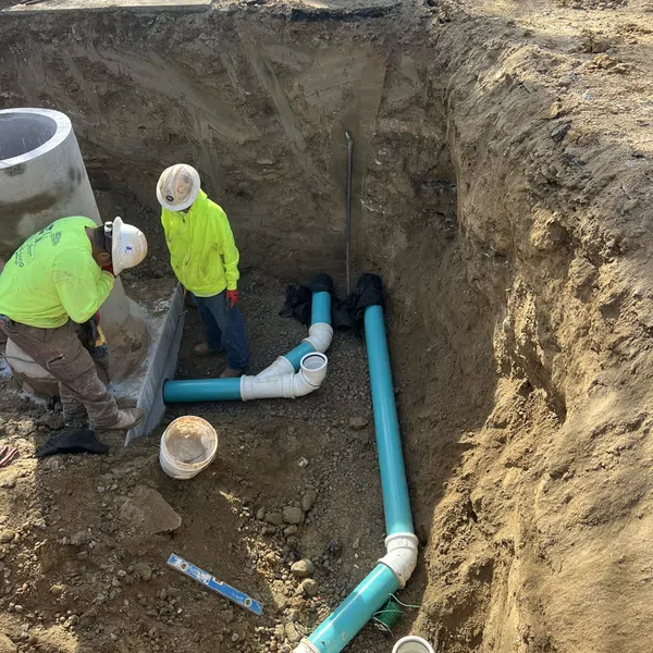 Construction workers install blue PVC pipes in a deep excavation trench on a construction site.