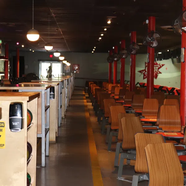 Interior of a bowling alley with wooden seats, ball racks, and hanging ceiling lights in rows.