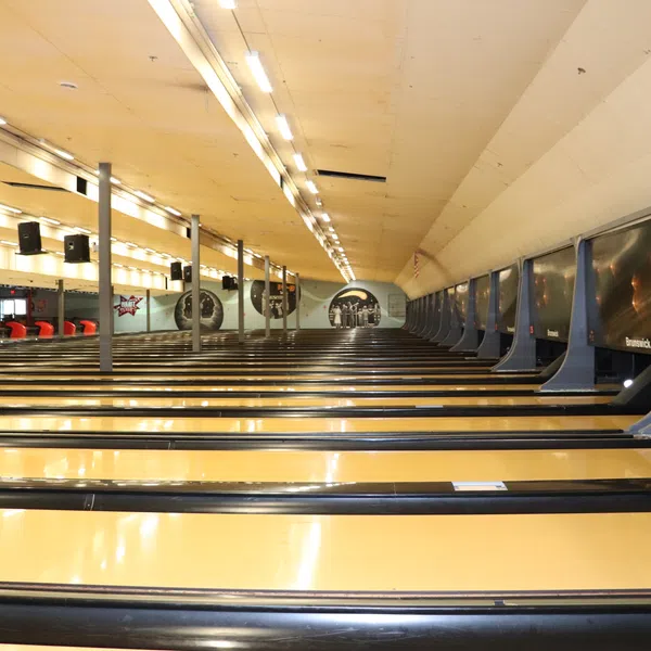 Interior view of an empty bowling alley with multiple polished lanes and overhead lights.