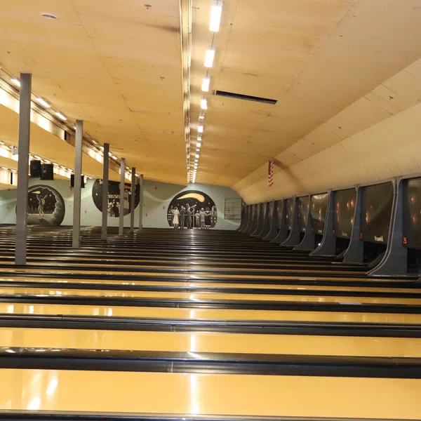 Wide view of an empty bowling alley with multiple polished lanes and overhead lights.