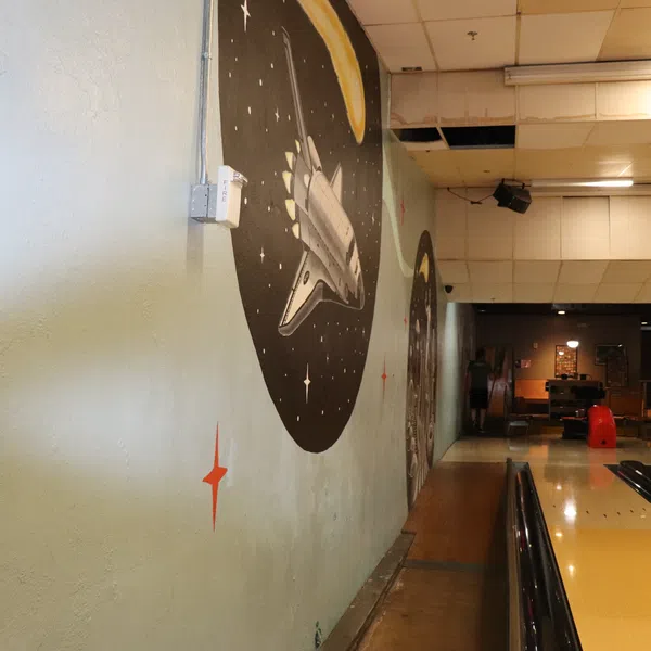Bowling alley with space-themed mural featuring a space shuttle and stars along the wall beside lanes.