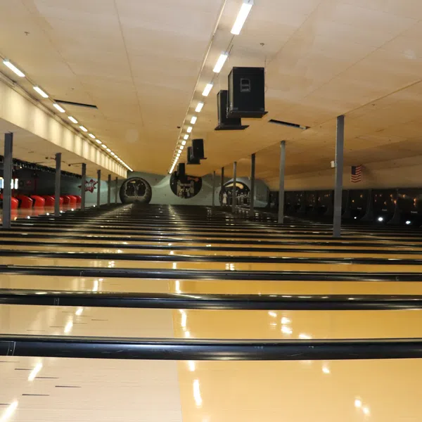 Interior view of an empty bowling alley with multiple lanes and red seating along the side under bright lights.