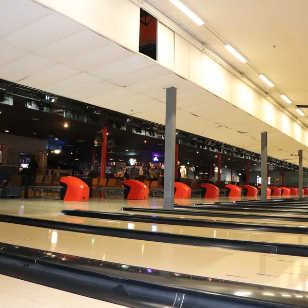 Empty bowling alley lanes with red seating and dimly lit interior under a bright ceiling.