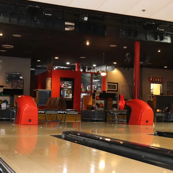 Interior view of a retro bowling alley with lanes, ball racks, and seating under dim lighting.