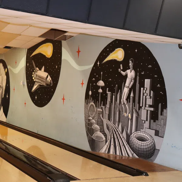 Wall mural at bowling alley featuring space themes, futuristic city, astronaut, space shuttle, and cosmic elements.