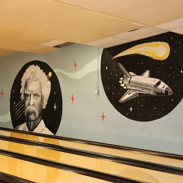 Mural of a man with white hair and mustache, space shuttle, and comet on bowling alley wall