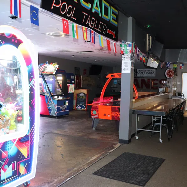 Indoor arcade with claw machine, air hockey table, pool tables, and international flags hanging from ceiling.