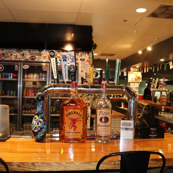 Bar countertop with Fireball whiskey and Tito's vodka bottles, beer taps, and glasses in a cozy pub setting.
