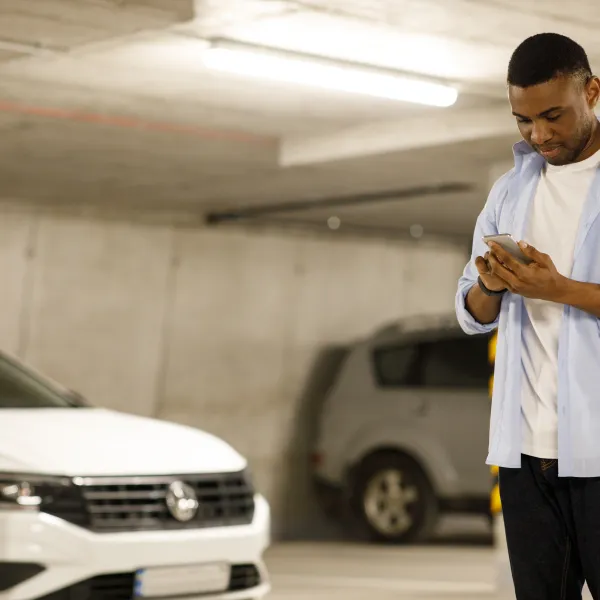 Man standing in parking garage using smartphone with cars parked in the background under fluorescent lighting