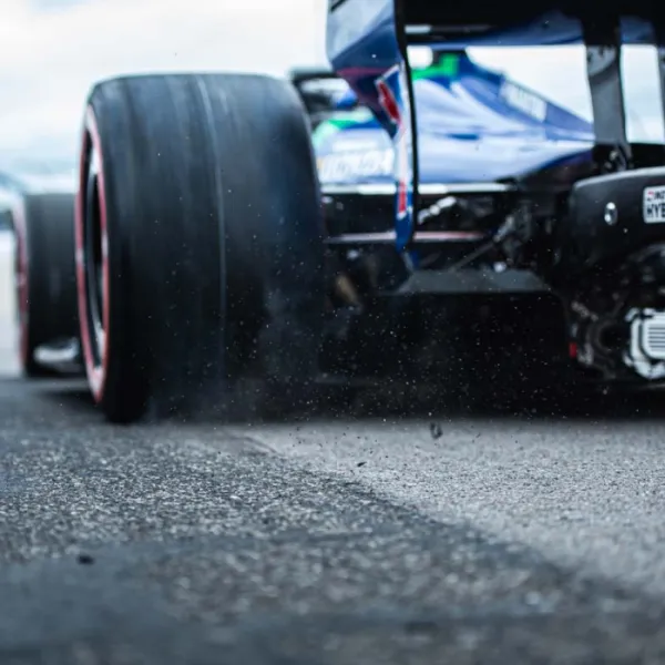 Close-up of a Formula 1 race car rear tire kicking up debris on asphalt track during a race event.