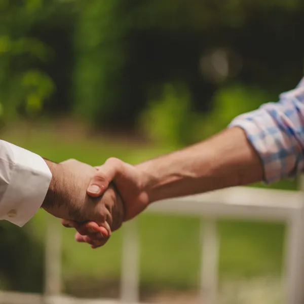 Close-up of two people shaking hands outdoors with blurred greenery in background.