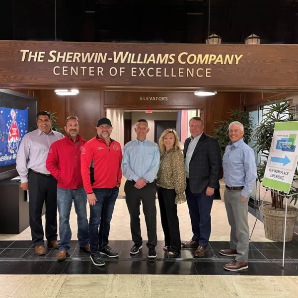Group of seven professionals standing under Sherwin-Williams Company Center of Excellence sign inside office building.