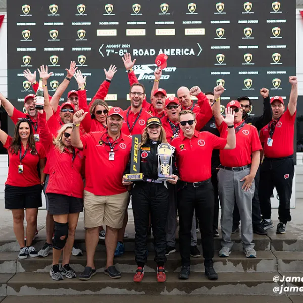 Group of racing team members in red celebrating with trophy at Road America race event in August 2021.