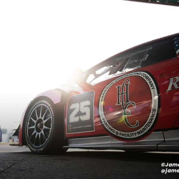 Low-angle close-up of red race car number 25 with sponsor logos and sun glare in background