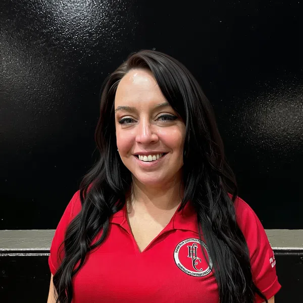 Smiling woman with long dark hair wearing a red polo shirt with a logo on black background.
