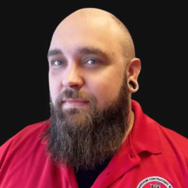 Bearded man with bald head and black ear gauges wearing red collared shirt against black background