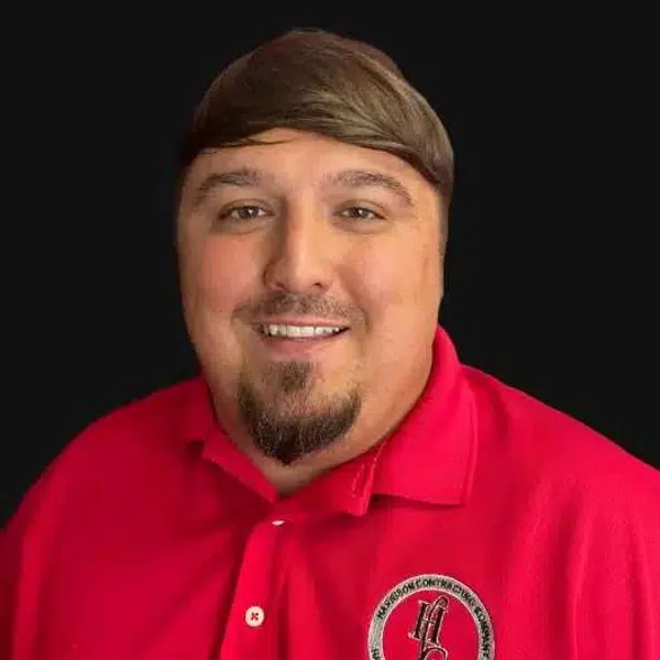 Smiling man wearing a red polo shirt with a contractor company logo on a black background.