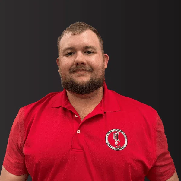 Man wearing a red polo shirt with a circular logo on a dark gray background, smiling and facing the camera.
