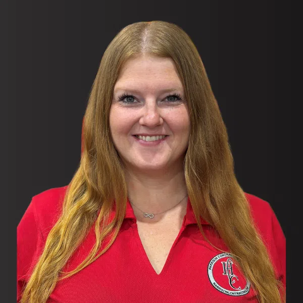 Smiling woman with long blonde hair wearing a red polo shirt with HCC logo on dark background.