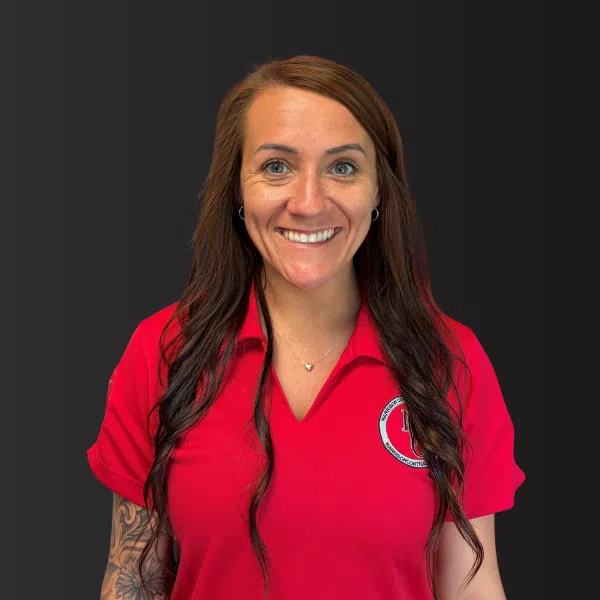 Smiling woman with long brown hair in red collared shirt with logo on dark background
