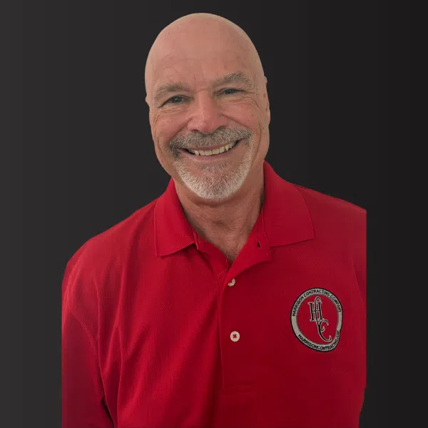 Smiling bald man with gray beard wearing a red polo shirt with an embroidered logo on black background