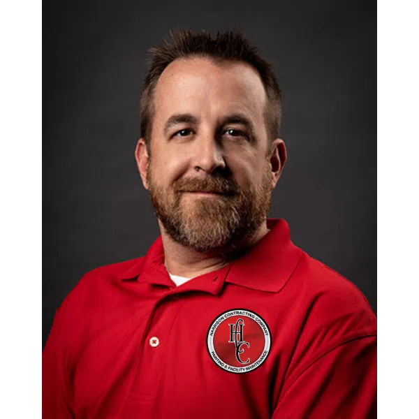 Portrait of a smiling man with a beard wearing a red polo shirt with a company logo on the chest.