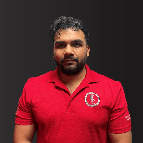 Man with dark curly hair and beard wearing a red polo shirt with embroidered logos on chest and sleeve.