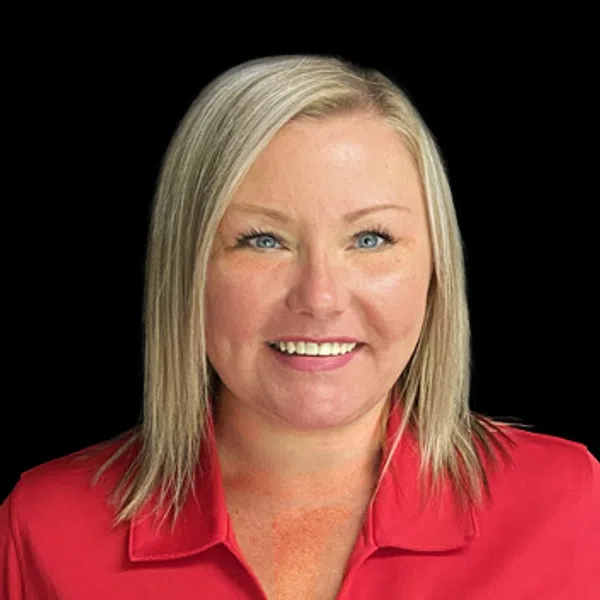 Smiling woman with blonde hair wearing a red collared shirt featuring a circular company logo against a black background