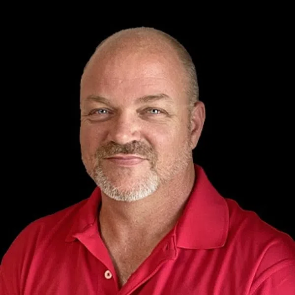 Portrait of a middle-aged man with a beard wearing a red polo with a logo on a black background