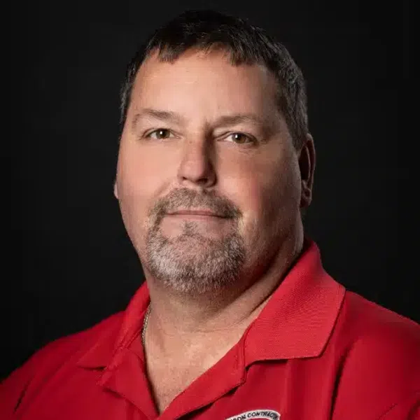 Middle-aged man with short dark hair and goatee wearing a red polo shirt against a black background