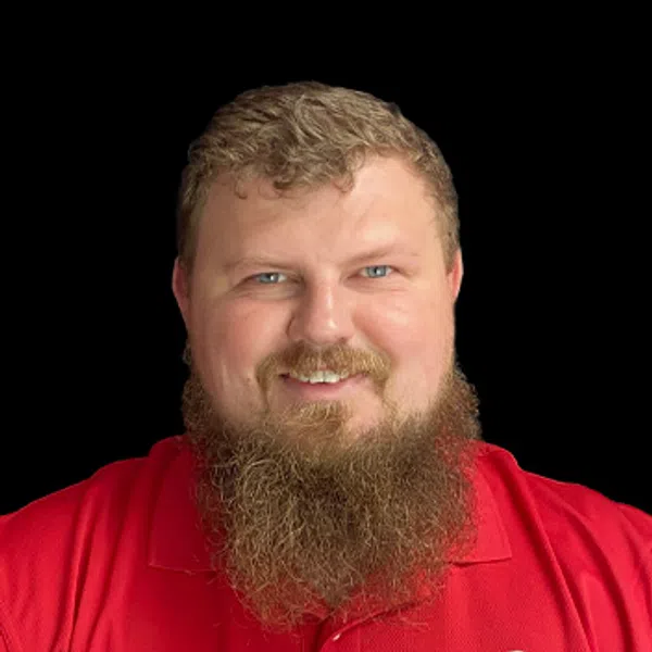 Smiling man with a full beard wearing a red polo shirt with a company logo on black background