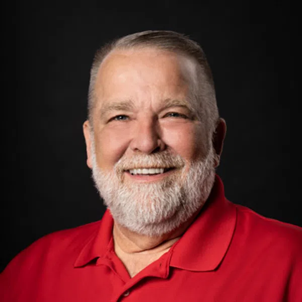 Smiling older man with white beard wearing a red polo shirt with a contractor company logo on black background