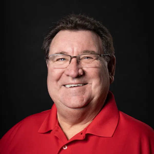 Smiling man wearing glasses and a red polo shirt with a construction company logo on black background.