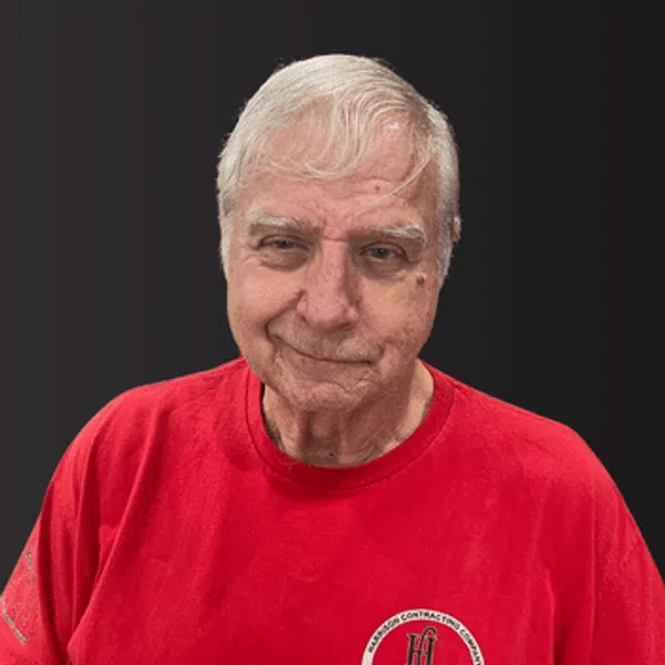 Elderly man with white hair wearing a red t-shirt with a circular logo on a black background