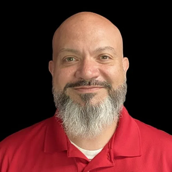 Smiling bald man with gray beard wearing a red polo shirt with a construction company logo on black background