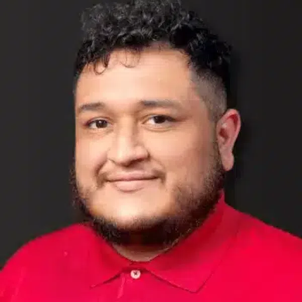 Man with curly hair and beard wearing a red polo shirt against a black background