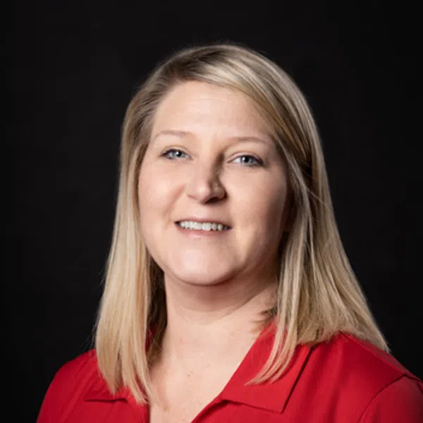 Smiling blonde woman wearing a red polo shirt with a company logo on a black background