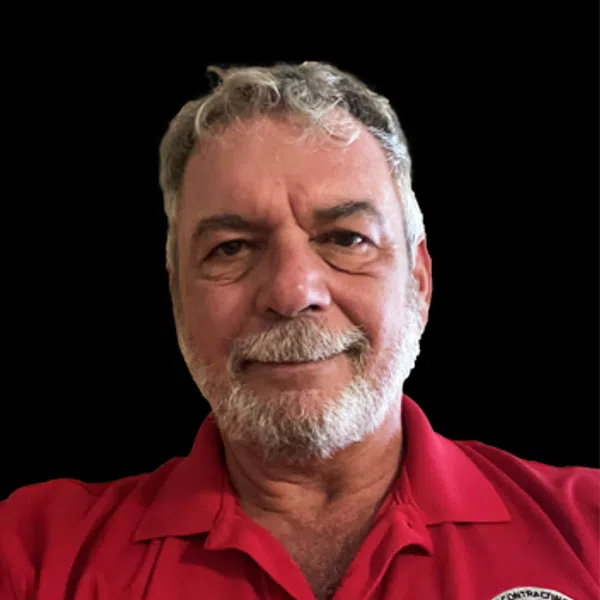 Older man with gray hair and beard wearing a red collared shirt with an embroidered circular logo on black background