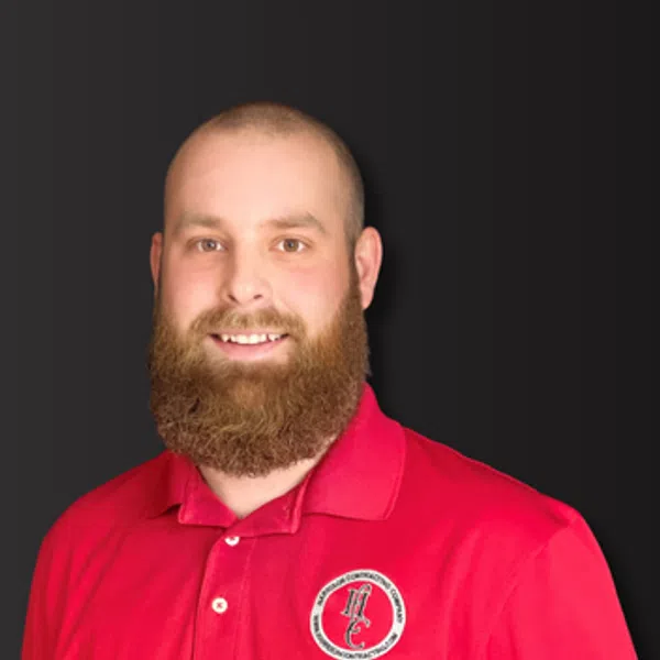 Smiling bearded man wearing a red polo shirt with a circular logo on a dark background.