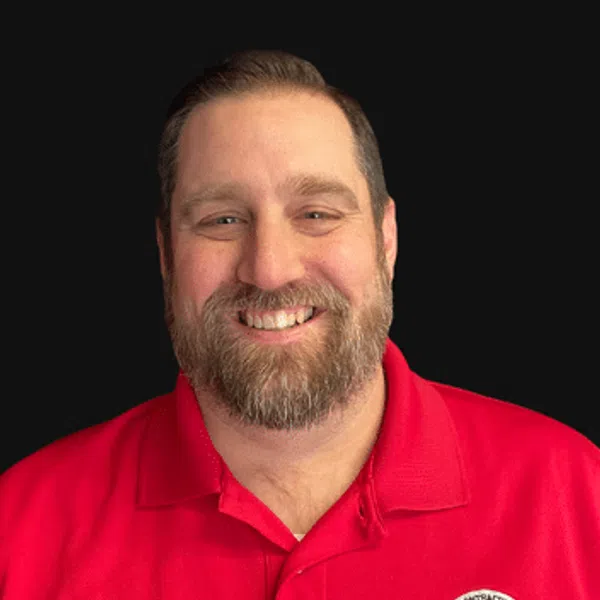 Smiling man with beard wearing a red polo shirt with a building contractor company logo on black background