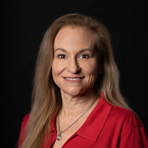 Smiling woman with long blonde hair wearing red shirt with a circular logo on black background