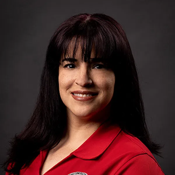 Woman with dark hair wearing red polo shirt with business logo on chest and sleeve against dark background