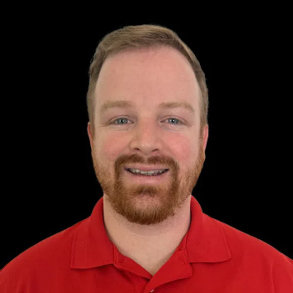 Smiling man with red hair and beard wearing a red polo shirt with a construction company logo on black background