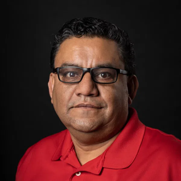 Middle-aged man with glasses wearing a red polo shirt with a logo on black background