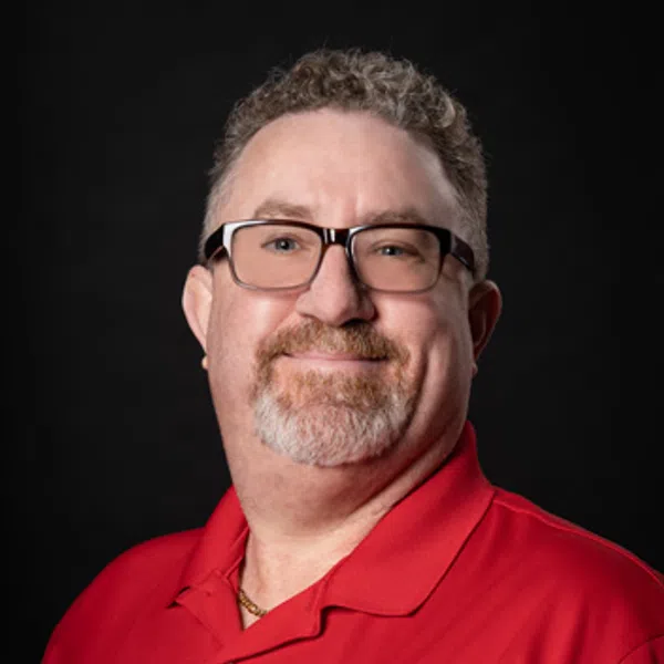 Smiling middle-aged man with glasses wearing a red polo shirt with a company logo on black background