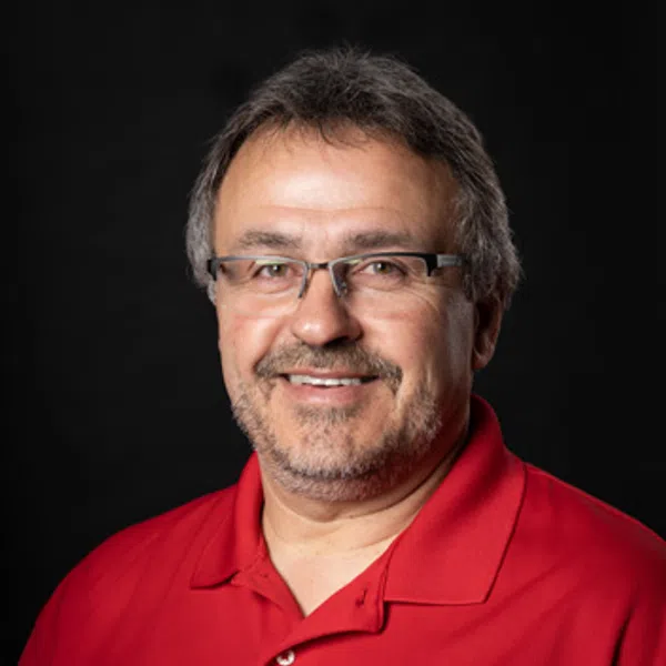Middle-aged man with glasses wearing a red polo shirt with an embroidered company logo, smiling against black background