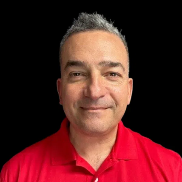 Smiling man with short gray hair wearing a red polo shirt with a circular logo on black background